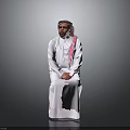 Man In Traditional White Robe With Pink Headscarf Sitting On Gray Background