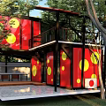 Two Story Container Building With Red Containers Yellow Circles And Outdoor Deck Surrounded By Trees