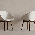 Two Modern Dining Chairs with Beige Upholstered Curved Backrest and Wooden Legs Against Light Wall