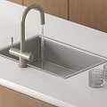 Modern Kitchen Sink with Silver Faucet Water Flowing and Glass Cups on White Countertop