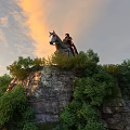 Ancient Warrior on Horseback Standing Atop Hilltop With Green Trees and Sunset Sky