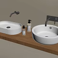 Oval And Round White Washbasins On Wooden Countertop With Wall Mounted Faucets And Soap Dispensers