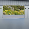 Open Gray Metal Roller Door Revealing Yellow Flowers Green Vegetation And Gray Paved Ground