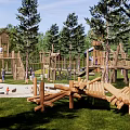 Outdoor Children's Playground With Log Climbing Structures Slide Green Lawn And Surrounding Trees