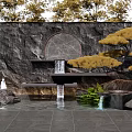 Stone Garden Wall with Circular Ornament Waterfall Feature Yellow Pine Tree Rocks And Green Plants