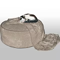 Round Beige Ottoman With Black And White Cat Sleeping On Beige Blanket Draped On Floor