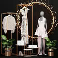 Mannequin Wearing Pink Asymmetrical Dress With Golden Display Rack Green Plants And Decorative Lights