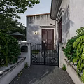 Black Wrought Iron Entrance Gate With Dark Wooden Door And Green Plants Near White Wall