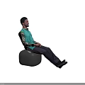Man In Green Shirt With Camouflage Sleeves Sitting On Black Stool Hands Clasped Gray Background
