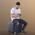 Man in white T-shirt and ripped jeans sitting on gray cylindrical object using smartphone