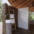 Hotel Room With Thatched Roof Wooden Bed Green Plants Stone Wall And Tiled Floor