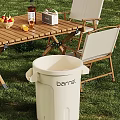 Outdoor White Plastic Barrel Trash Can Near Wooden Table With Foldable Chairs On Grass