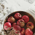 Fresh Red Apples in Wooden Bowl Alongside Books Candles and Dried Flowers on Marble Countertop