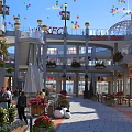 Vibrant Commercial Street with Colorful Balloons Outdoor Seating Green Plants and Pedestrians