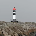 Red And Black White Lighthouse Tower Standing On Rocky Coastal Area