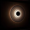 Modern Circular Wall Lamp With Layered Rings And Central Sphere On Wooden Panel