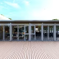 Modern Building Exterior With Large Glass Doors Wooden Deck And Green Trees Under Blue Sky