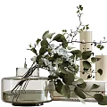 Transparent Glass Vase With White Flowers And Green Leaves Next To White Candles And Books