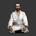 Man In White Judo Uniform Sitting Cross Legged On Dark Background With Beard