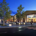 Vibrant Commercial Street With Modern Glass Buildings Trees Pedestrians And Night Lighting