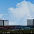Outdoor Basketball Court With Blue Sky White Clouds Green Grass Wire Mesh Fence And Billboard