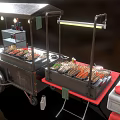 Grilled Skewers At Food Stall With Multiple Trays Red Chairs Black Tables And Condiment Bottles