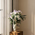 White Vase with Purple Irises White Flowers and Green Leaves on Wooden Table Near Curtain