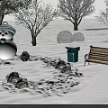 Snow Covered Trees in Winter Park Scene With Snowman Wooden Bench And Green Trash Can