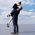 Romantic Couple Moment Man Lifting Woman In Suit And Black Dress Against Blue Sky