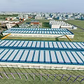 Aerial View of Industrial Factory Buildings With Blue Roof Panels Surrounded by Green Fields