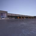 Gray Exterior Industrial Warehouse Featuring Yellow Trucks Spacious Front Yard Trees And Flags At Entrance