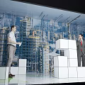 Two men discussing large white block models against industrial city backdrop