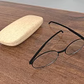Beige Glasses Case And Black Eyeglasses Placed On Wooden Table Top