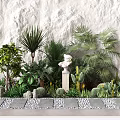Assorted Flowers And Green Plants With Decorative Statues On Stone Pathway Against Stone Wall