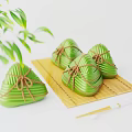 Traditional Green Zongzi Tied with Brown String on Bamboo Mat with Bamboo Leaves and Chopsticks