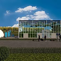 Industrial Factory Building with Glass Facade in Green Outdoor Area Under Blue Sky and Clouds