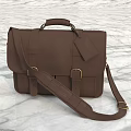 Brown Leather Briefcase with Adjustable Shoulder Strap Attached Tag and Metal Buckles on Marble Surface