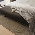 Black Footstool With Plaid Blanket Beside Bed On Wooden Floor And Woven Rug
