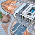 Aerial View of Modern Apartment Building with Parking Lot and Surrounding Roads Near Open Land