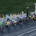 Various Colored Bicycles and Motorcycles Parked Outdoor With Green Grass Wet Ground and Billboard
