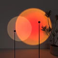 Modern Floor Lamp With Circular Orange Red Light Projection Against Gray Wall And Potted Plant