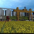 Industrial Plant With Silos Yellow Gantry Crane Truck And Yellow Flowers Field Under Blue Sky