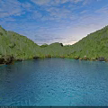 Calm Blue Lake Surrounded by Lush Green Forested Hills and Cloudy Sky With Stone Shores