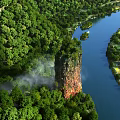 Aerial View Of Lush Green Forest With Winding Blue River And Tall Red Rock
