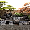 Serene Garden Landscape With Tiered Waterfalls Rocks Green And Orange Trees And Wooden Fence
