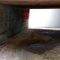 Abandoned Tunnel With Graffiti Covered Concrete Walls Dirt Floor And Bright End Light