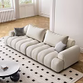 Beige Three-Seater Sofa With Plush Rounded Cushions White Walls Windows And Round Coffee Table