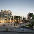 Evening Commercial Street Scene with Circular Building Palm Trees Water Feature and Ferris Wheel