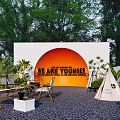 Feature Wall With Orange Circle Text Surrounded By Plants Tables Chairs And Teepee In Garden