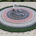 Modern Circular Water Fountain with Colorful Paving and Green Plant Surroundings